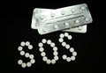 White pills on black background, which forming the word SOS and blisters, prescription drugs dependence, dependency concept Royalty Free Stock Photo