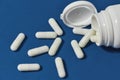 White pills, capsules scattered from a white bottle, jar on a blue background Royalty Free Stock Photo