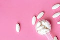 White pills in dosage spoon for drugs on a pink background, close-up