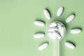 White pills in dosage spoon for drugs in the shape of a flower on a green background, close-up Royalty Free Stock Photo