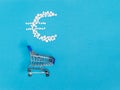 White pills in euro sign shape over shopping cart on blue background. Pharmaceutical concept of medical expenses Royalty Free Stock Photo