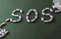 White pills on green background, which forming the word - SOS, with a blister of pills on background. Royalty Free Stock Photo