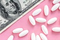 White pills with money on a pink background, medicine flat lay with copy space, rising cost of health care Royalty Free Stock Photo