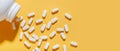 White pills are poured from a jar on a yellow background. Food supplement, multivitamins, medications.
