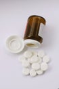 White pills spilled from fallen pill bottle. Top view of pills and medicine container lying on white background illustrating drug Royalty Free Stock Photo