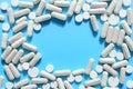 White pills, tablets and capsules frame on a blue background with copy space. Drugs, medicines, pharmaceutical mockup. Drug prescr