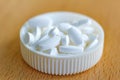 White pills in a white plastic bottle cap on the table closeup