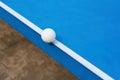 White pingpong ball hits the edge of blue pingpong table