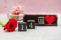 On a white and pink background, there is a rose, a heart, a gift and a calendar made of cubes with the date of February 14.
