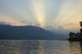 A white pink lines of a sunset in the evening blue sky over the lake and silhouettes of mountains