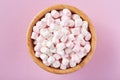 White and pink marshmallows in wooden bowl on pink background
