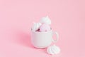 White and pink twisted meringues in a small porcelain coffe cup on pink background. French dessert prepared from whipped with