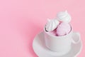 White and pink twisted meringues in a small porcelain coffe cup on pink background. French dessert prepared from whipped with