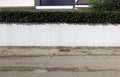 White plaster fence with low hedge above. Tiled concrete sidewalk and street in front