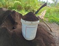 white plastic barrel containing ground manure. around it is a pile of fertilizer and two hoes