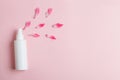White plastic bottle of floral facial moisturizing toner or rose hair spray and petals isolated on pastel pink background