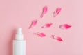 White plastic bottle of floral facial moisturizing toner or rose hair spray and petals isolated on pastel pink background