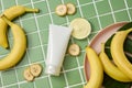 A white plastic bottle unbranded decorated with ripe bananas and banana slices on green tile background. Royalty Free Stock Photo