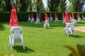 white plastic chairs, tables, and red sun umbrellas on green grass. Pool yard. Poolside. hotel resort