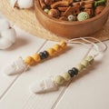 White plastic clothespin with white, black and orange wooden beads on white laces for baby pacifiers near wooden bowl. Royalty Free Stock Photo