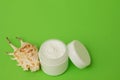 White plastic cosmetic jars and white open cream on a green background