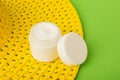 White plastic cosmetic jars and white open cream on a green background