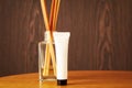 White plastic cosmetic tube with cream and wooden perfume sticks on the table