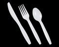 White plastic knife, fork and spoon on black background.