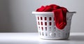 White plastic laundry basket filled with clean clothes including a red sweater and sock on a white surface with gray background Royalty Free Stock Photo