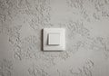 A white plastic light switch is mounted on a textured gray wall. The switch has a simple Royalty Free Stock Photo