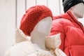 White plastic mannequin in a red knitted beret and light down jacket