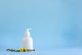 White plastic mockup bottle dispenser with flowers of healing herb foalfoot or Tussilago farfara on lighnt blue empty background