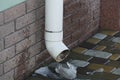 White plastic pipe on brown brick wall above wet sidewalk Royalty Free Stock Photo