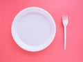 White plastic plate and fork on pink background, flat lay, top view. Bright minimalistic concept of eating and table setting. Royalty Free Stock Photo
