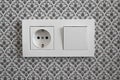 White plastic switched double socket. Light switch and power socket control panel on wall with wallpaper, close-up. Electrical