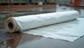 White plastic tarp roll rests on wet ground at construction site after rain. Waterproof material protection for building Royalty Free Stock Photo