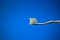 White plastic toothbrush with light blue toothpaste. Close up studio shot, isolated on blue background, no people Royalty Free Stock Photo