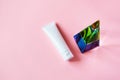 White plastic tube mockup with moisturizer cream, shampoo or facial cleanser and glass pyramid prism on pink background