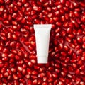 White plastic tube with pomegranate cream on red ripe garnet seeds. Natural organic cosmetic product packaging design, branding Royalty Free Stock Photo