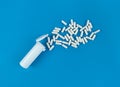 White plastik medical bottle and scattered pills capsules on blue backdrop with copy space