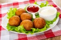 White plate with bowl of ketchup, mayonnaise, small fried pies on lettuce on napkin on wooden table