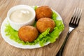 White plate with bowl of mayonnaise, round fried pies on lettuce, fork on wooden table