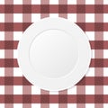 White plate on a brown checkered tablecloth. Empty dish on a kitchen table cloth.