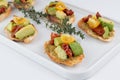 On a white plate bruschetta with pesto sauce, sun-dried and fresh tomatoes, avocado