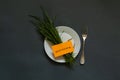 White plate a bunch of green grass and a fork on the table and next note good morning in English