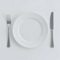 A minimalist setting of a white plate with a fork and knife on a light gray background Royalty Free Stock Photo