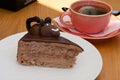 White plate with chocolate piece of cake with cream and edible chocolate mouse on top of it beside of cup Royalty Free Stock Photo