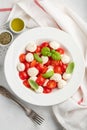 White plate of classic delicious caprese salad with ripe tomatoes, mozzarella and fresh basil leaves on gray concrete background. Royalty Free Stock Photo