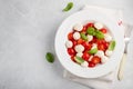 White plate of classic delicious caprese salad with ripe tomatoes, mozzarella and fresh basil leaves on gray background. copy spac Royalty Free Stock Photo