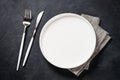 White plate, cutlery and napkin on black table top view. Royalty Free Stock Photo